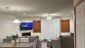 A modern living room with a dining area, a flat-screen TV mounted on the wall, and a ceiling fan. - Perfect 3-bedroom condo in beautiful Lake Placid for your getaway (Lake Placid)