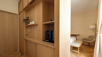 A modern, compact room with built-in wooden cabinets, a coffee machine, and a small seating area with a chair and table.