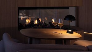 A modern interior with a round wooden table, two wine glasses, and a black lamp. - Le N°3 par Champagne Thiénot (Reims)