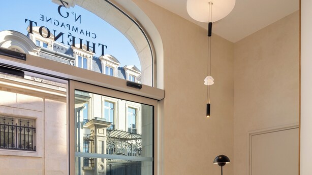 A reception area with a glass door leading to a courtyard, a sign for 'No 3 Champagne Thi énot', and a modern interior design. - Le N°3 par Champagne Thiénot (Reims)