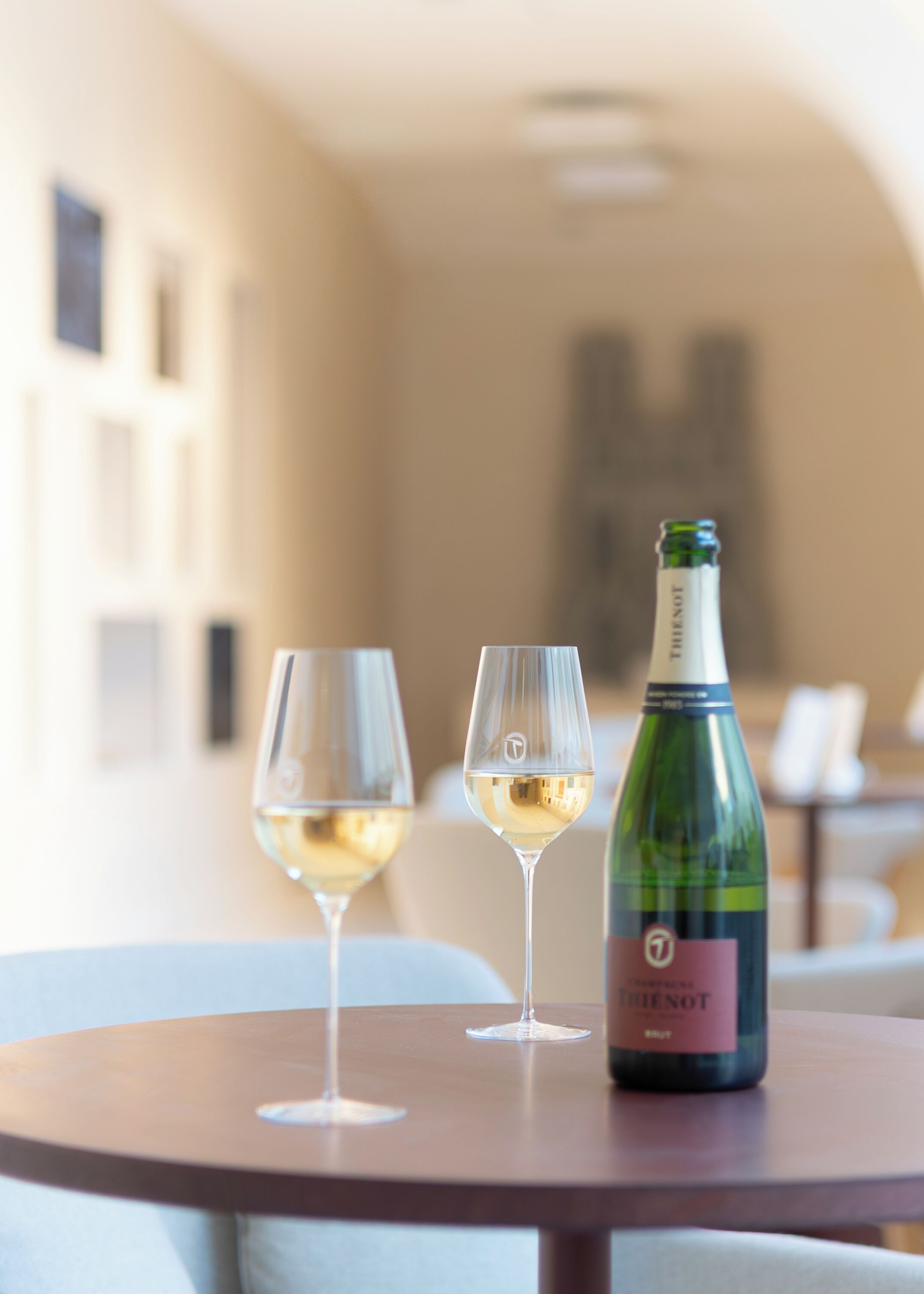 Een fles wijn en twee glazen op een ronde tafel in een kamer met een neutraal kleurenpalet en een modern design.