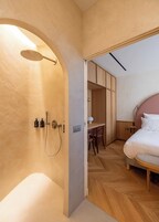 Ein modernes Schlafzimmer mit Holzboden, einem Bett mit weißer Bettwäsche, einem Schreibtisch mit Stuhl und einem begehbaren Kleiderschrank.