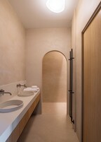 A narrow bathroom with two sinks, a mirror, and a wooden door.