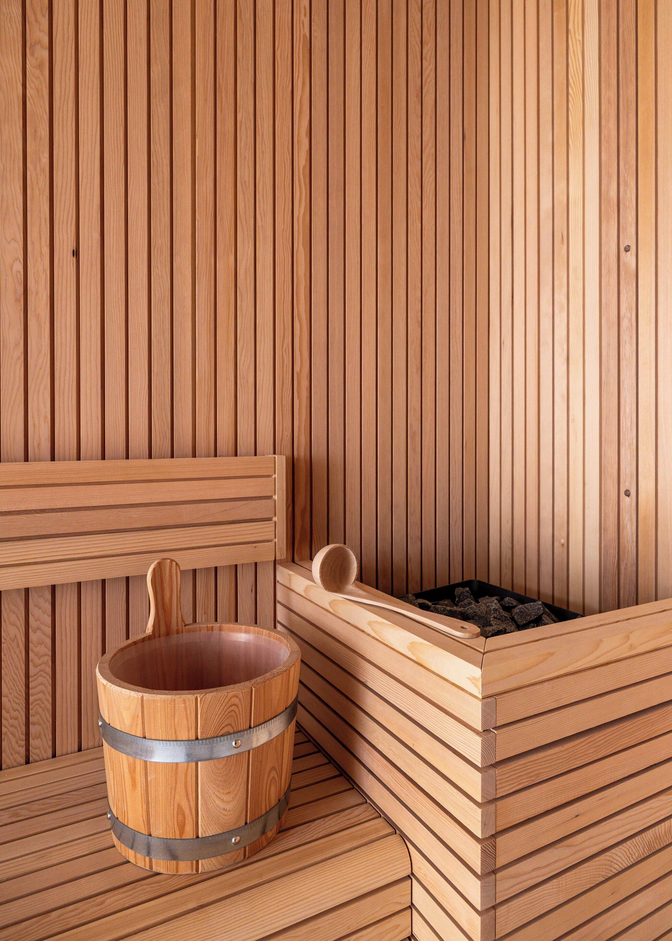 Een houten sauna met een houten bad, een houten bank en een houten bak met een metalen band.
