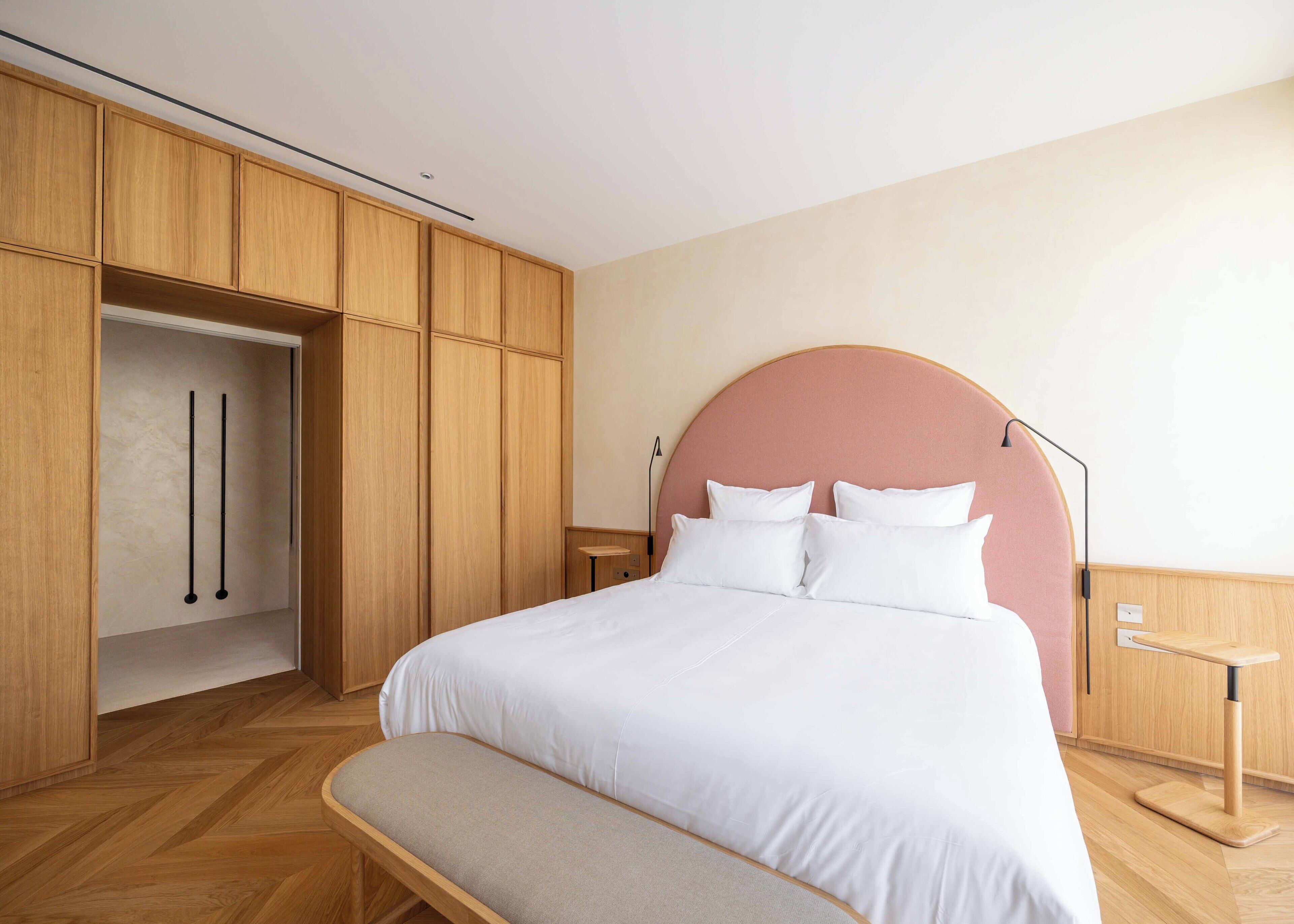 Un dormitorio con una cama grande, un banco, un armario de madera y un cabecero redondo.