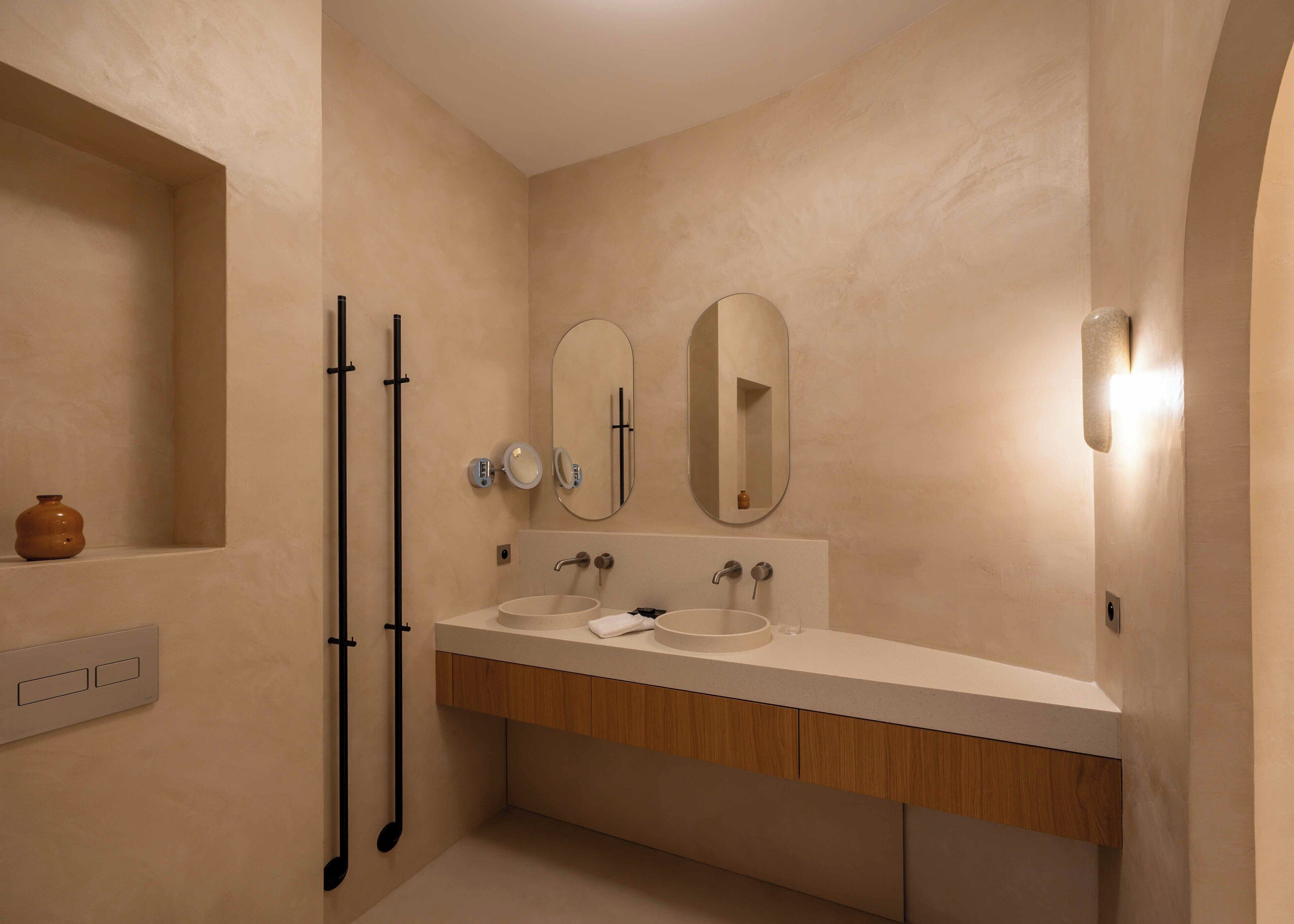 Un bagno con doppio lavandino, due specchi, un portasciugamani e un piccolo ripiano con un vaso.
