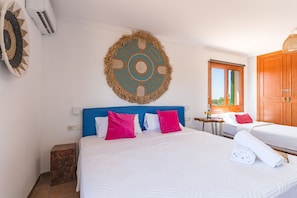 A hotel room with a bed, a blue headboard, a woven wall hanging, a wooden wardrobe, and a window with a view.