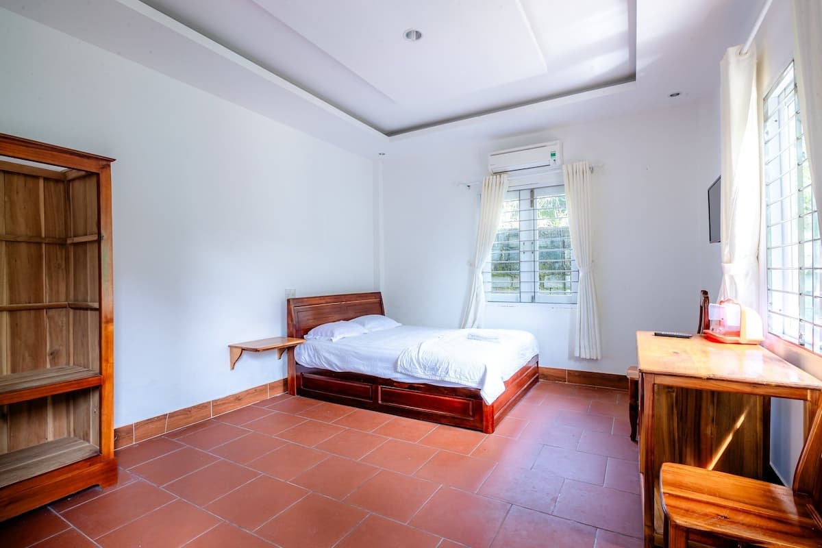 A bedroom with a wooden bed, a small bedside table, a wooden wardrobe, and a window with curtains.