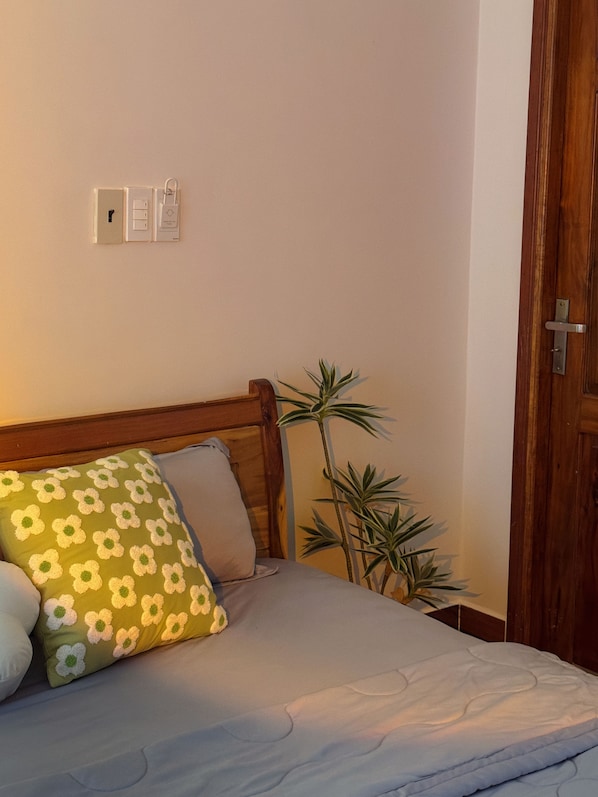 Un dormitorio con cama, planta en la mesita de noche y puerta de madera.