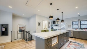 Een moderne keuken met een centraal eiland, hangende lampen en een uitzicht op de omgeving door grote ramen.