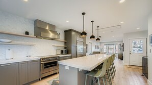 Een moderne keuken met roestvrijstalen apparatuur, een groot eiland en hangende lampen.