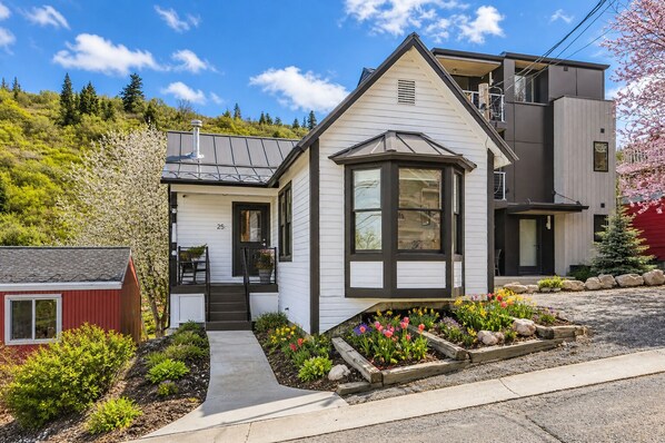 A two-story house with a front porch, a small attached garage, and a garden with flowers. - Elevation 25 Your Pet Friendly Basecamp for Adventure (Park City)