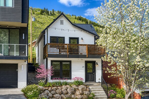 Ein zweigeschossiges Haus mit Balkon, Garage und einer Steinmauer mit Blumen.