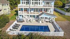 Uma casa grande, com vários andares, piscina, varandas múltiplas e áreas de estar ao ar livre.