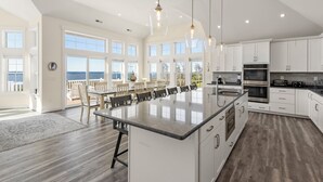 Uma cozinha espaçosa com uma ilha grande, armários brancos e vista para o oceano.