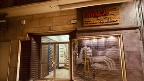 Ein Schaufenster mit einem Schild mit dem Schriftzug "MALA" und einer heruntergelassenen Metallrolltür.