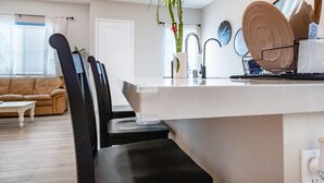 A modern kitchen with a central island, black chairs, a dining table, and a living area with a sofa and coffee table. - Spacious, Family-friendly Chula Vista 3BR + Children's Playroom+Pool & Park (Chula Vista)