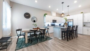 A modern kitchen with white cabinets, a central island, and a dining area with a table and chairs. - Spacious, Family-friendly Chula Vista 3BR + Children's Playroom+Pool & Park (Chula Vista)
