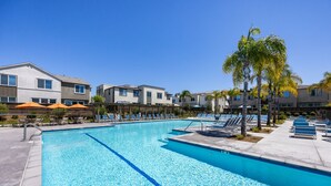 A swimming pool with clear blue water, surrounded by lounge chairs and umbrellas, and adjacent to multi-story buildings. - Spacious, Family-friendly Chula Vista 3BR + Children's Playroom+Pool & Park (Chula Vista)