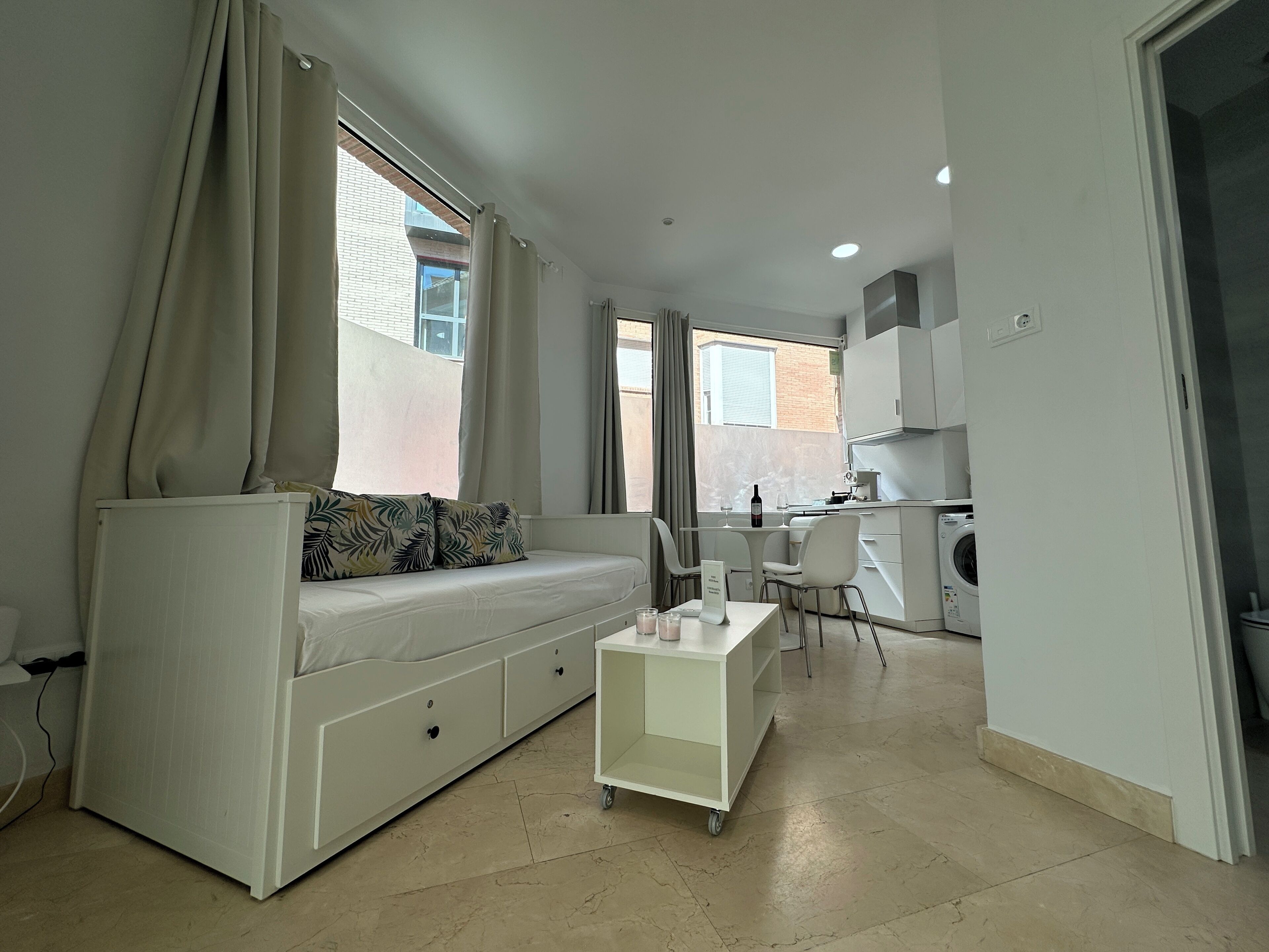 A compact living space with a sofa, a small dining table, and a kitchen area with a washing machine.