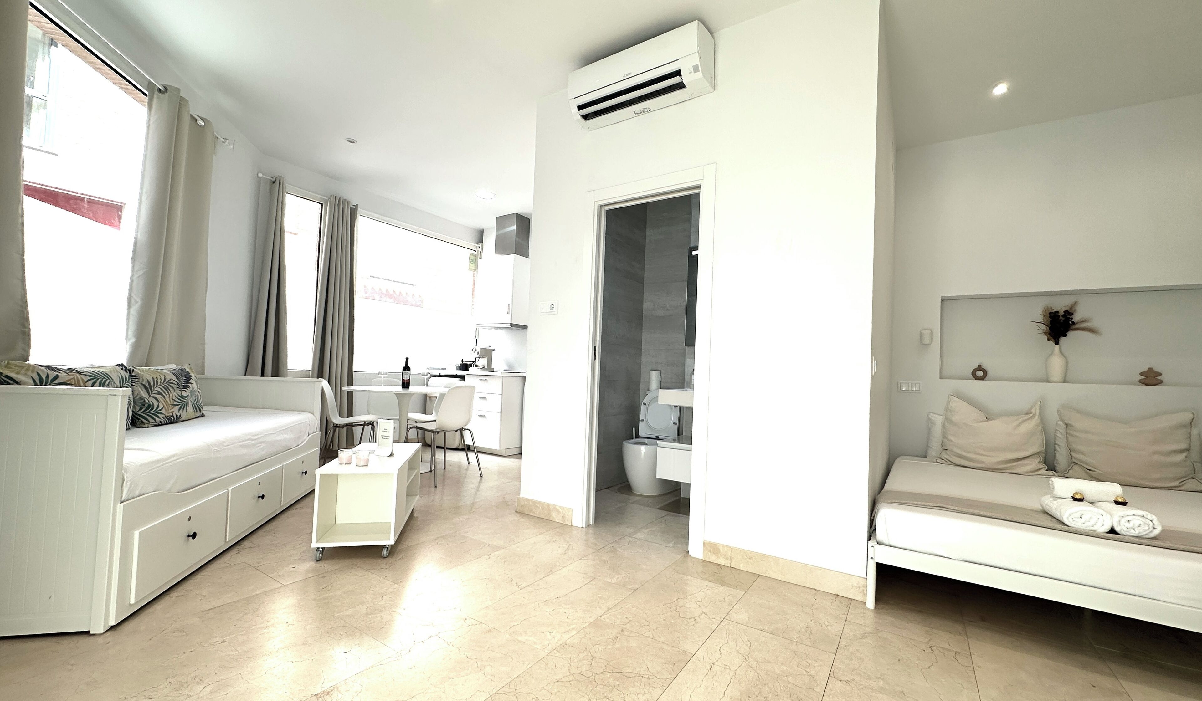 A modern, well-lit living room with a sofa, a dining area, and a separate bathroom.