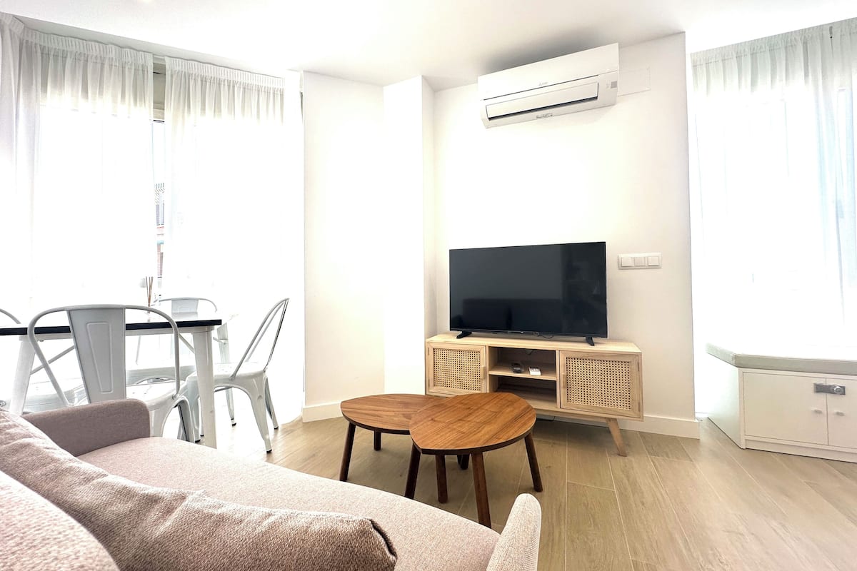 A modern living room with a flat-screen TV, a dining table, and a sofa.