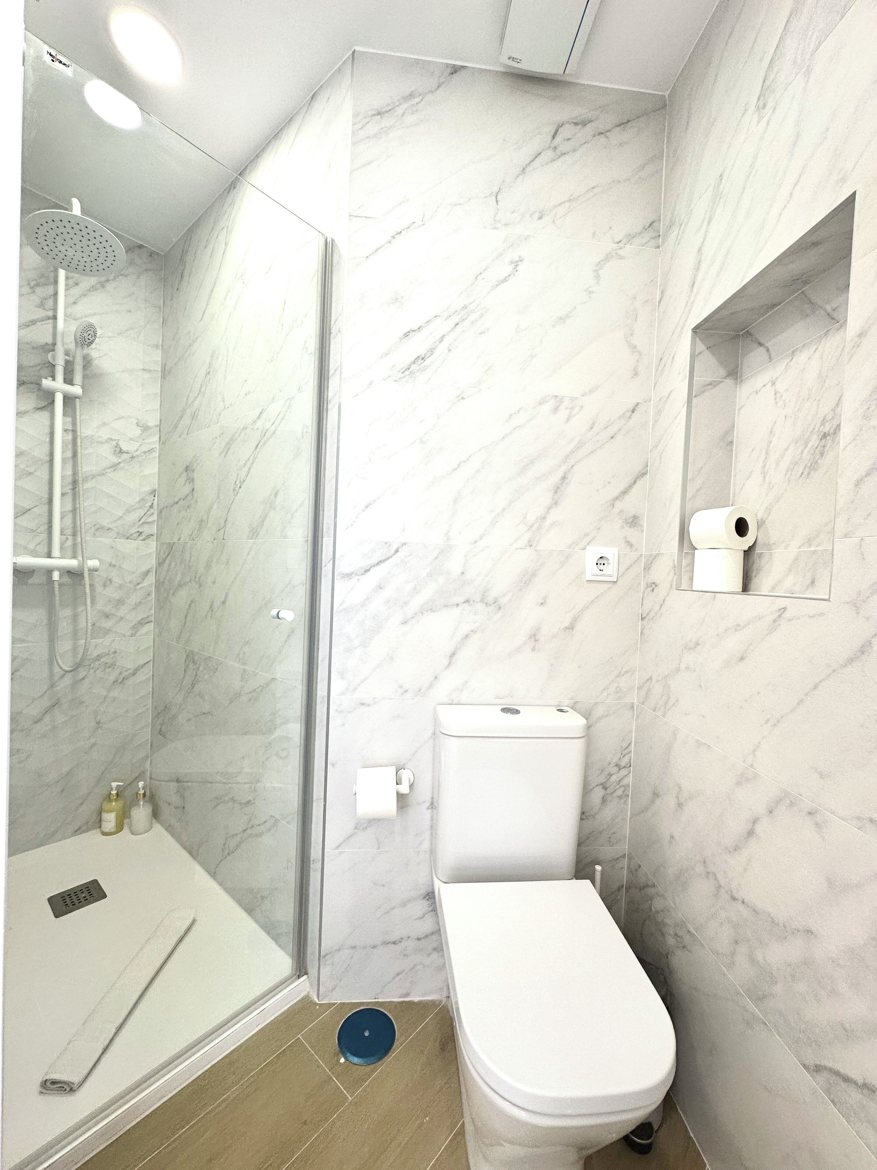 A bathroom with a shower, toilet, and marble walls.