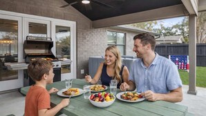 Una familia cena al aire libre con una parrilla y un porche cubierto.