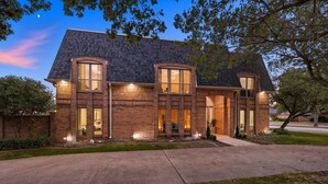 A two-story brick house with a dark shingled roof, large windows, and a well-maintained lawn. - 7BR 5BA w Pool, Hot Tub, Sport Court & Game Room (DeSoto)