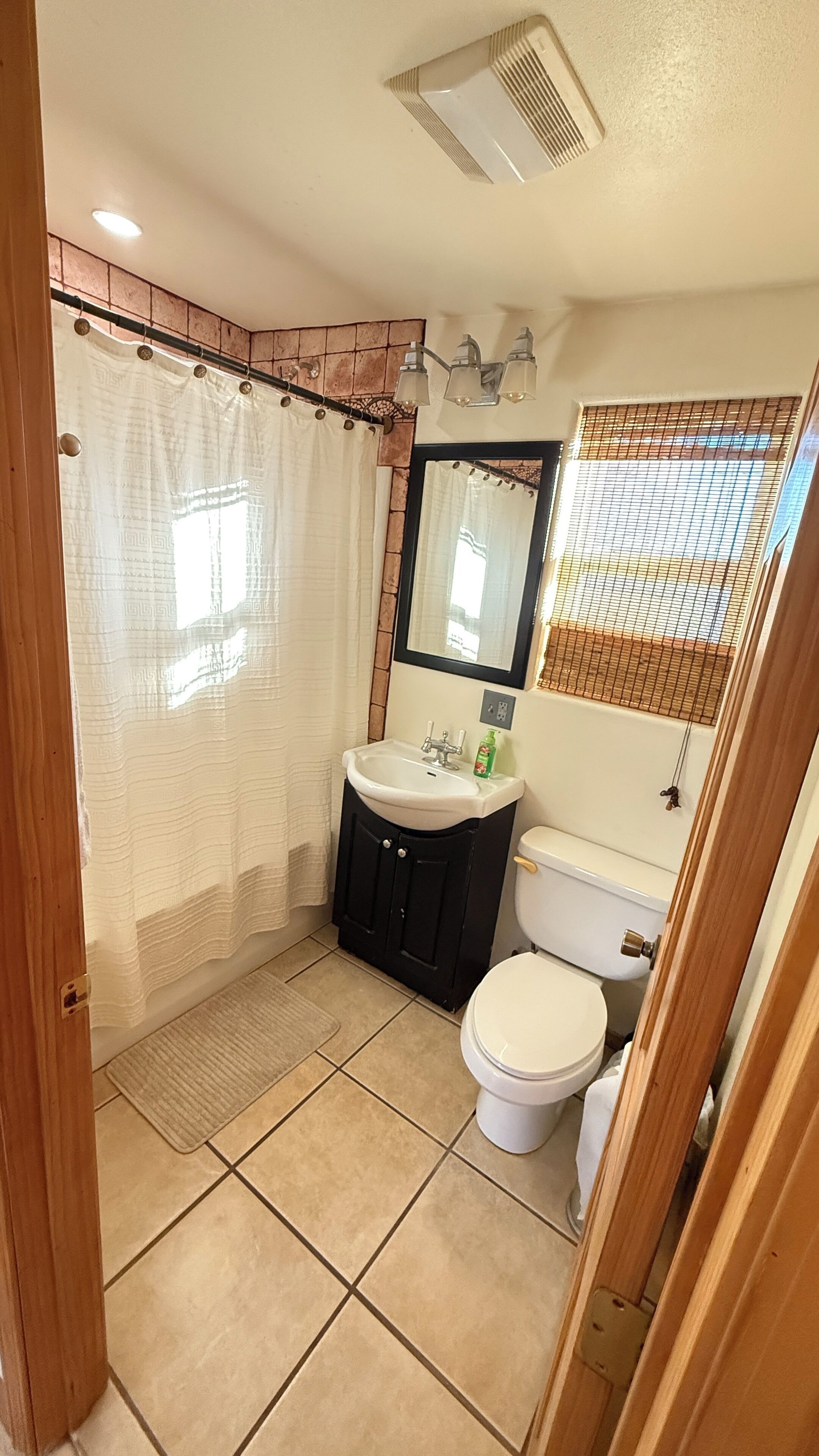 Een badkamer met douchegordijn, wastafel, spiegel, toilet en betegelde vloer.