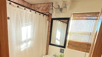 Een badkamer met douchegordijn, wastafel, spiegel, toilet en betegelde vloer.