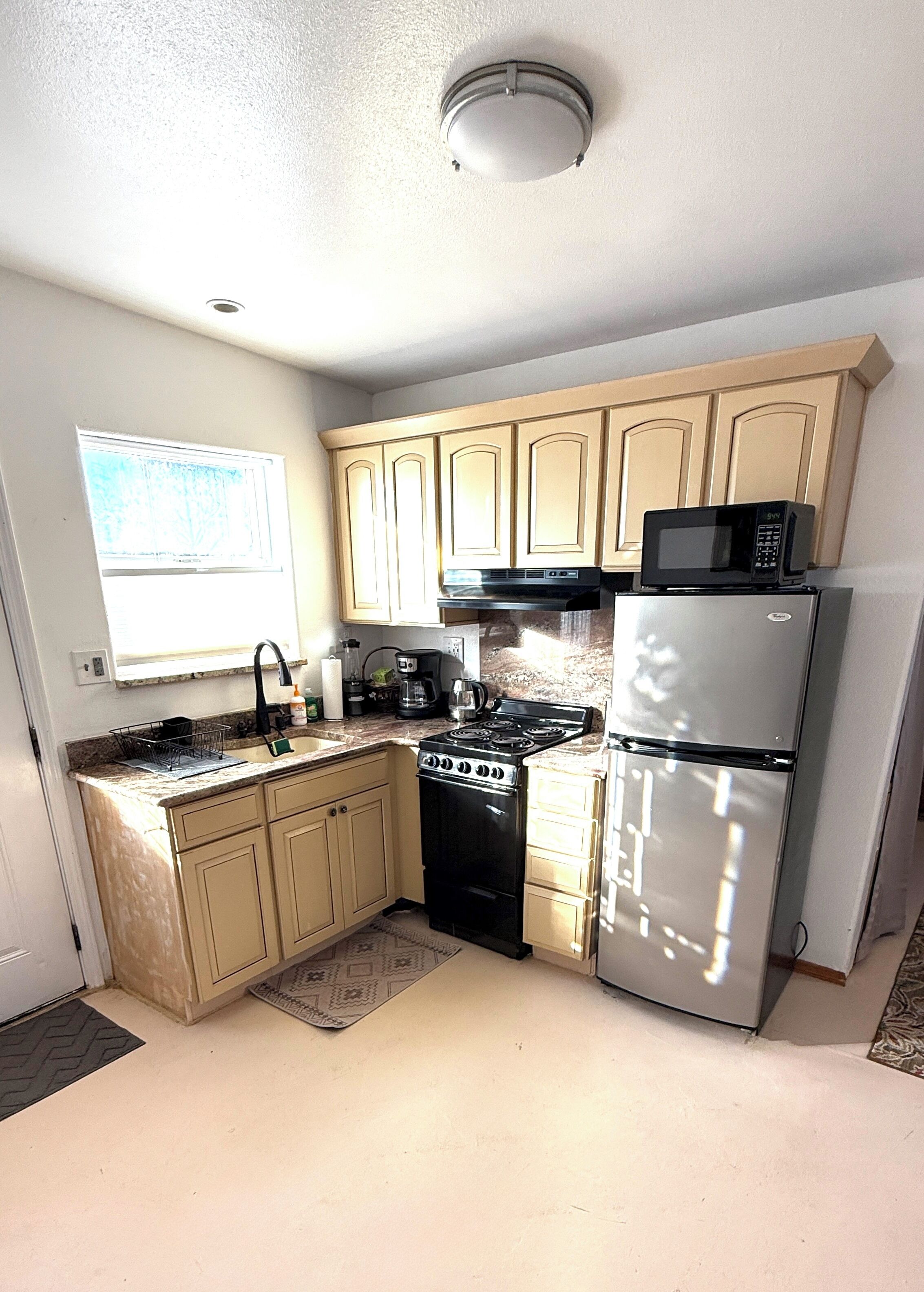 A kitchen with beige cabinets, a black stove, a silver refrigerator, and a microwave on top of the fridge.
