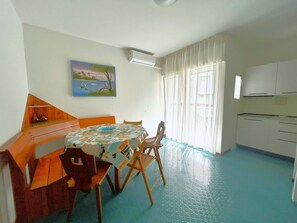 Une pièce comprenant une table à manger, des chaises, un tableau, un appareil de climatisation et un coin cuisine.