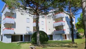 Un immeuble résidentiel à plusieurs étages, doté de balcons, d’un petit espace jardin et surplombant un ciel dégagé.