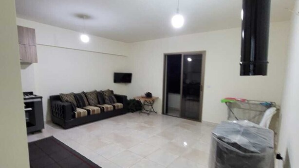 A spacious living room with a large sofa, a TV, and a sliding glass door leading to a balcony.