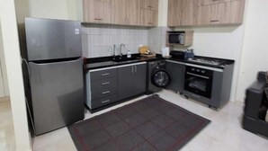 A compact kitchen with a refrigerator, microwave, stove, and cabinets.