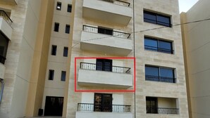 A multi-story residential building with balconies, stone steps, and a parked car.