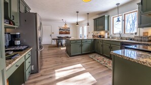 A spacious kitchen with green cabinets, a granite countertop, and a central island. - Spacious 5-bdrm house in tranquil 7 Devils. Hottub & AC. < 1 mile to Hawksnest (Seven Devils)