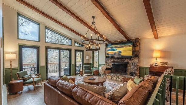 A spacious living room with a large brown leather sofa, a stone fireplace, and a television mounted on the wall. - Spacious 5-bdrm house in tranquil 7 Devils. Hottub & AC. < 1 mile to Hawksnest (Seven Devils)