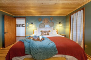 Une chambre avec un plafond en bois, un lit avec une literie rouge et blanche, une couverture bleue tricotée et des éléments de décoration murale.