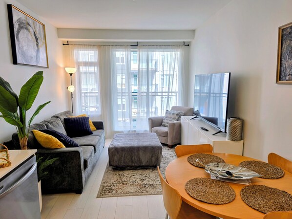A modern living room with a grey sofa, ottoman, and a dining table with woven placemats.