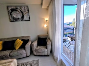 A living room with a sofa, armchairs, a painting, a lamp, and a view of a balcony.