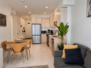 A modern kitchen with a stainless steel refrigerator, wooden cabinets, and a dining area with a round table and chairs. - Central Surrey Gem – Steps from SkyTrain, Dining & Groceries (Surrey)