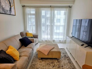 A living room with a sofa, ottoman, and a TV on a cabinet.