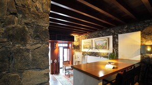 Une cuisine rustique avec un îlot central en bois, des murs en pierre et un coin repas comprenant des chaises et un tapis.