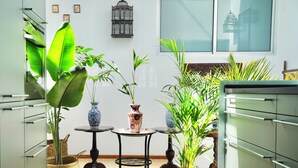 Une cuisine compacte dotée d’appareils électroménagers modernes, un petit coin repas avec deux tables et diverses plantes en pot.