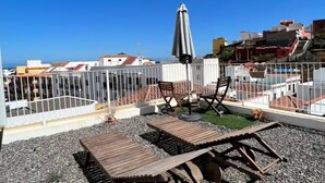 Une terrasse sur le toit, avec des fauteuils de jardin en bois, une table et un parasol.