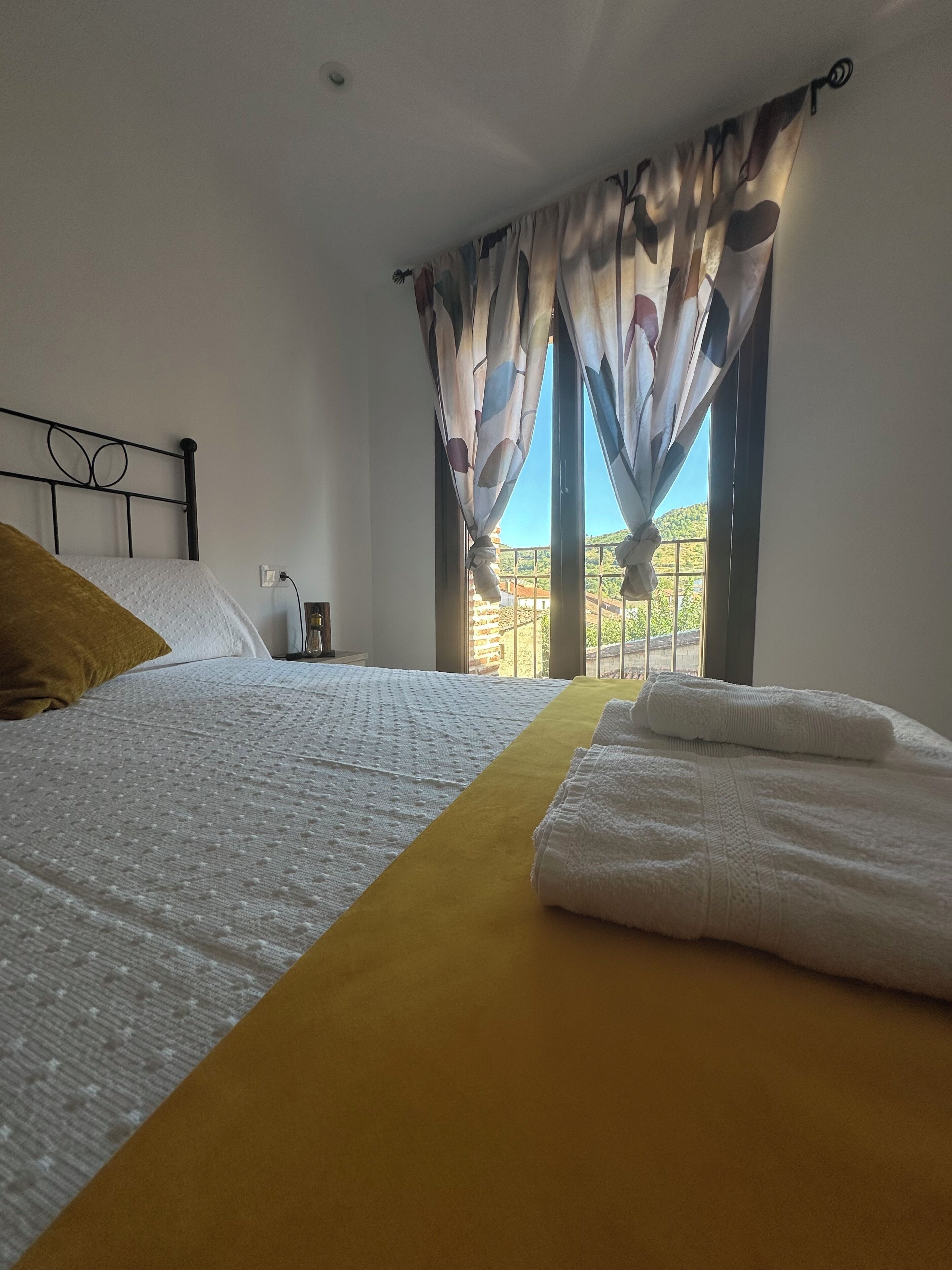 A hotel room with a bed, a window with curtains, and a view of the outside.