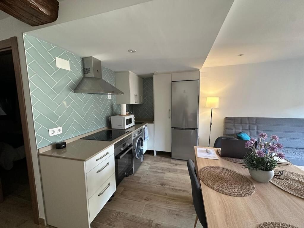 Une cuisine compacte équipée d’un four à micro-ondes, d’une cuisinière et d’un lave-linge, un coin repas avec une table et des chaises, et un canapé gris.