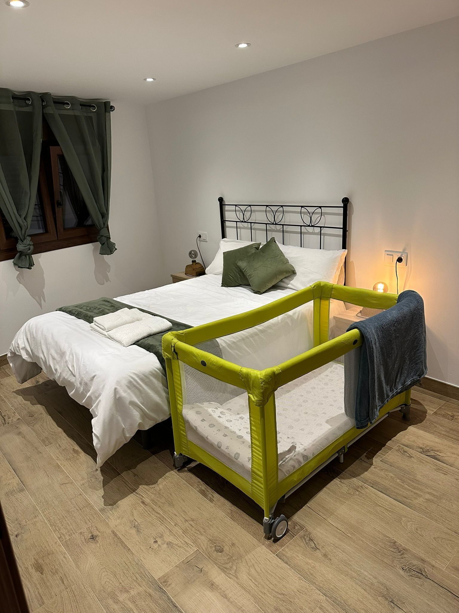 Un dormitorio con cama, un barandal de seguridad verde, una mesita de noche y una ventana con cortinas.